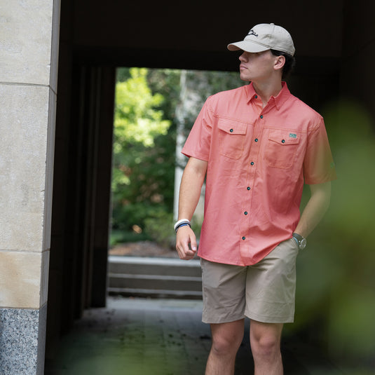 A man in the Drake Frat Gingham Check Button-Down Short Sleeve Shirt. Features include UPF30 sun protection, moisture-wicking fabric, and two chest pockets. Ideal for outdoor activities.