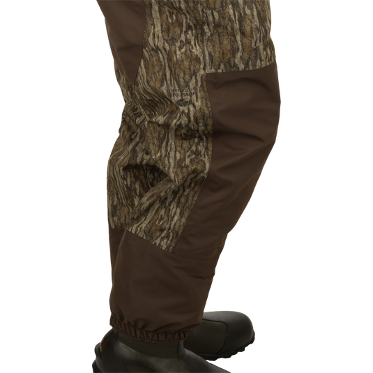 A close-up of the Youth Insulated Guardian Elite Vanguard Breathable Wader, featuring a person's leg with a camouflage pattern, pants, jacket, and shoe.
