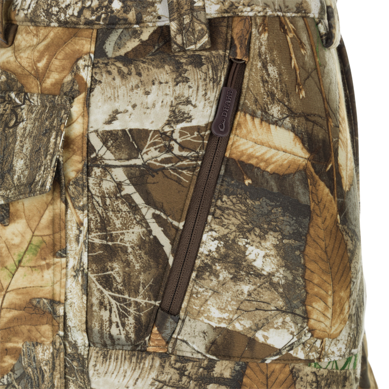 MST Microfleece Softshell Pant - Realtree: Close-up of camouflage pants with zipper, leaf pattern fabric, and logo. Wind-resistant, moisture-repellent, scent control technology. Comfortable fit, articulated knees, and side zips for easy movement. Slash, cargo, and security pockets.