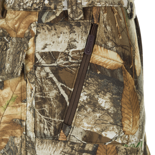 MST Microfleece Softshell Pant - Realtree: Close-up of camouflage pants with zipper, leaf pattern fabric, and logo. Wind-resistant, moisture-repellent, scent control technology. Comfortable fit, articulated knees, and side zips for easy movement. Slash, cargo, and security pockets.