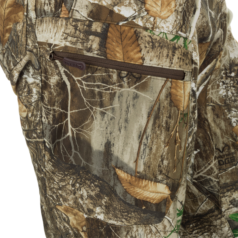 MST Microfleece Softshell Pant - Realtree: Close-up of camouflage pants with zipper, leaf, and fabric details. Superior protection and comfort with wind-resistant face fabric, 4-way stretch, microfleece lining, and DWR treatment. Agion Active XL® scent control technology. Side-elastic waist, gusseted crotch, articulated knees, and side zips for easy movement. Zippered pockets for storage.