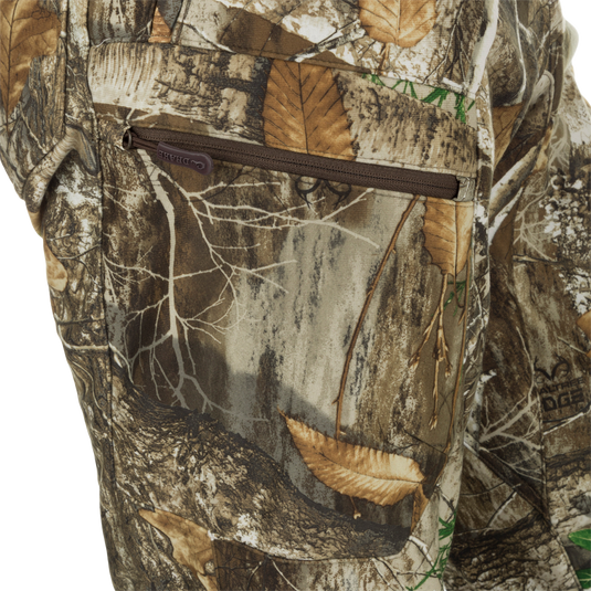 MST Microfleece Softshell Pant - Realtree: Close-up of camouflage pants with zipper, leaf, and fabric details. Superior protection and comfort with wind-resistant face fabric, 4-way stretch, microfleece lining, and DWR treatment. Agion Active XL® scent control technology. Side-elastic waist, gusseted crotch, articulated knees, and side zips for easy movement. Zippered pockets for storage.