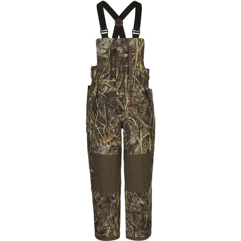 A product image of the EST Guardian Elite™ Bib Shell Weight, featuring a camouflage overalls with straps, perfect for hunters needing protection in any weather conditions. Made with 100% waterproof/windproof/breathable fabric and reinforced knees, seat, and wear areas. Adjustable shoulder straps, chest pockets, and fleece-lined handwarmer pockets provide convenience and comfort. Ideal for use in a ground blind.