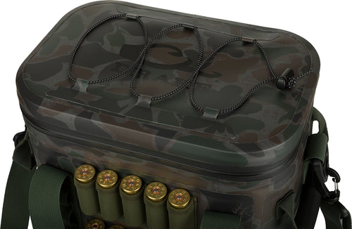 A close-up of the 16-Can Waterproof Soft-Sided Insulated Cooler by Drake Waterfowl. The rugged bag features molded handles, a padded shoulder strap, and molded feet for protection. It has a shock cord lashing strap with a cord lock on top and Molle loops on the front and back. Perfect for outdoor adventures.