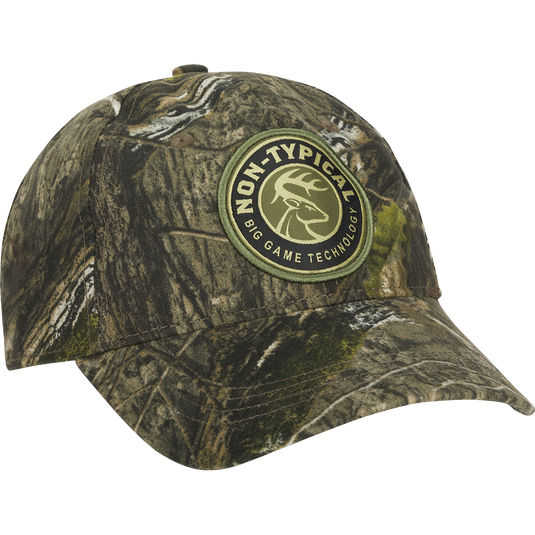 A close-up of the Big Game Technology Patch Camo Twill Cap, featuring a camouflage hat with a logo and a patch. The cap is made of 60% cotton/40% polyester, with a six-panel construction and a snap closure.