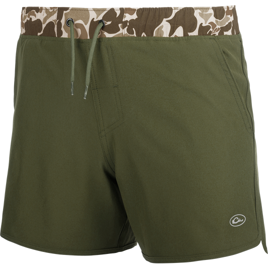 A pair of green camo-print shorts with a 5 inseam, built-in liner, and quick-drying fabric. Features scalloped hem, back pockets with hidden zippers, front slash pockets, and an elastic waistband with drawstring. Perfect for playground or beach wear. From Drake Waterfowl.