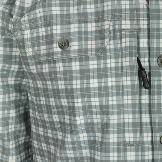 Hunter Creek Check Plaid Shirt L/S: Close-up of shirt button, black zipper pull, and pocket. High-performance, lightweight fabric with moisture-wicking and UPF30 sun protection. Functional features include hidden button-down collar, vented back cape, and chest pockets with Magnattach and zipper closures. Sculpted hem with built-in sunglass wipe. Adjustable roll-up sleeves. Perfect for hunting and outdoor activities.