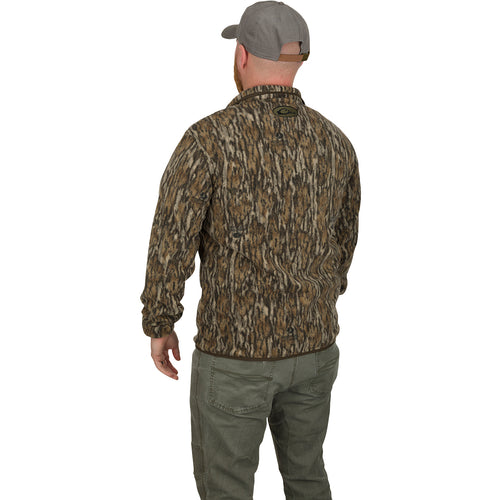 A man wearing the MST Camo Camp Fleece ¼ Placket Pullover, a camouflage jacket, hat, and pants, stands outdoors.
