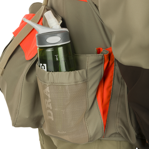 McAlister Upland Strap Vest: Person wearing a jacket with water bottle pockets, cargo pockets, and a game bag for hunting necessities.