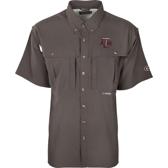 Texas A&M S/S Flyweight Wingshooter: A grey shirt with a logo, designed for warm-weather outdoor activities. Made of ultra-lightweight polyester fabric that dries quickly and wicks moisture away. Features include UPF 50+ sun protection, vented back, chest pocket, and zipper pocket.