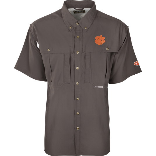 Clemson S/S Flyweight Wingshooter: A grey shirt with an orange logo and tiger paw patch. Made of ultra-lightweight polyester for quick-drying and breathability. Features include UPF 50+ sun protection, vented back design, Magnattach™ chest pocket, and vertical zipper pocket. Ideal for warm-weather outdoor activities.
