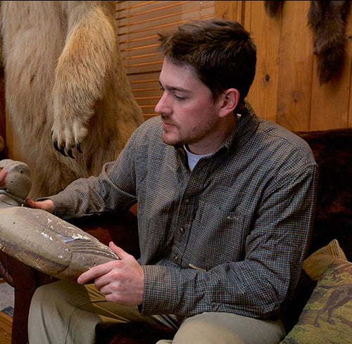 A man sitting in a chair holding a fake animal, wearing the Autumn Brushed Twill Shirt from Drake Waterfowl.