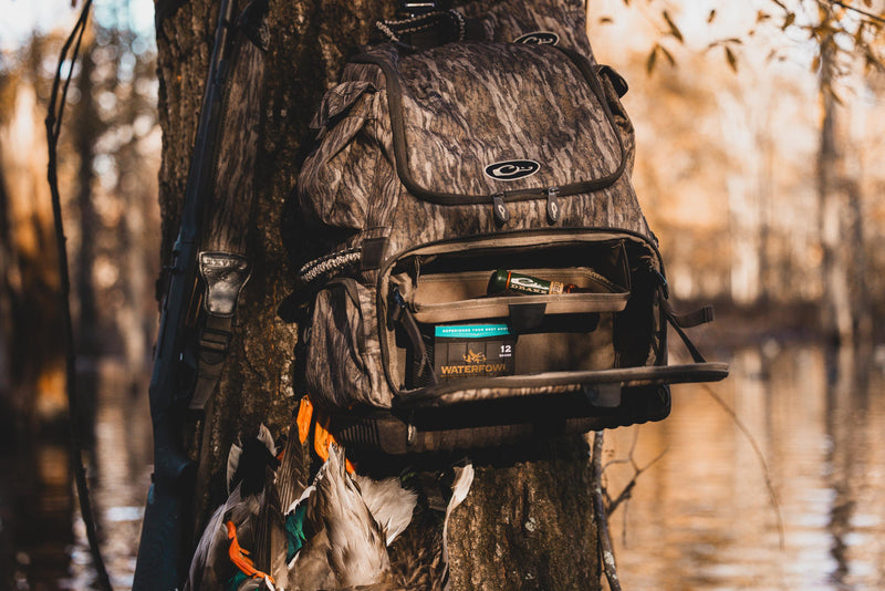 Tree Hugger Timber Pack with camo pattern, open to show Waterfowl shotgun shells, shotgun, and harvested ducks, demonstrating its rugged design and ample hunter storage features.