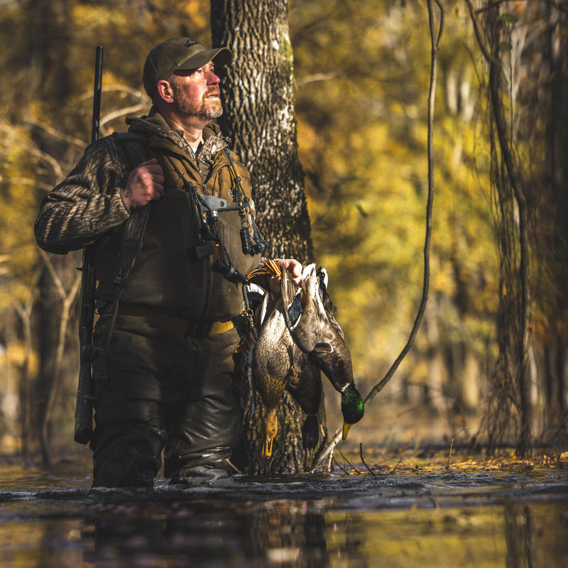 Hunter in marsh, wearing MST Endurance Quarter Zip Jacket with Hood, holding ducks and shotgun. Emphasizes mobility and breathability for outdoor pursuits.
