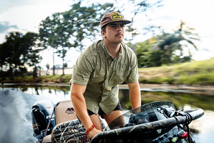 Young man steering a boat, wearing the Drake Cinco Ranch Western Acid Washed Short Sleeve Shirt, showcasing its classic western fit and functional design elements.