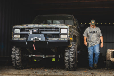 Make Boat Ramps Great Again T-Shirt worn by a man beside a lifted off-road truck, highlighting its rugged appeal and support for boat ramp restoration.