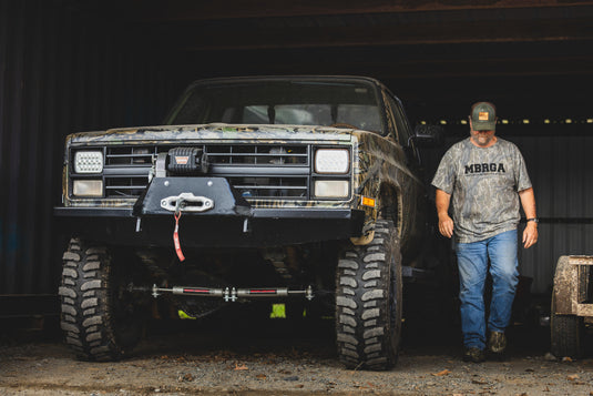 Make Boat Ramps Great Again T-Shirt worn by a man beside a lifted off-road truck, highlighting its rugged appeal and support for boat ramp restoration.