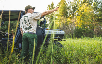Wearing the Nontypical Non-Typical Lightweight Breathable SWT Pant with Scent Control, a person stands by an off-road vehicle in a grassy field, ready for sunny outdoor adventures.