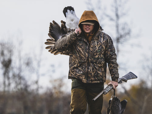 Hunter in camouflage with the LST BMF 3-in-1 Pit Jacket, carrying geese and a shotgun, showcasing durable, versatile hunting gear from Drake Waterfowl.