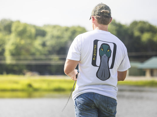 A person seen from behind wears a white Spoonie Logo T-Shirt featuring a graphic of a duck bill while fishing.