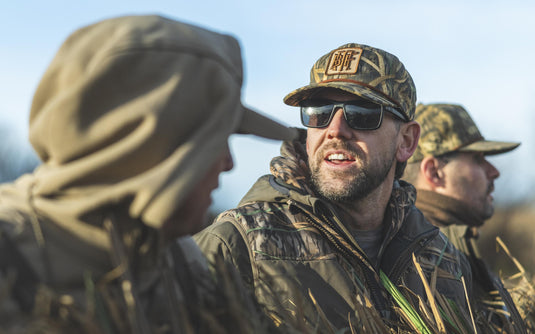 Three men wearing outdoor gear and Drake x Lost Hat BMF Goat Rope Caps outdoors.
