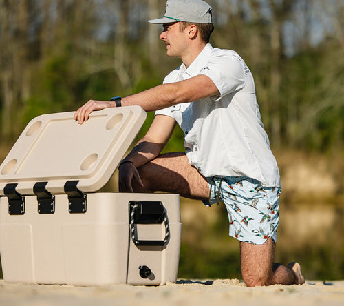 Man kneeling on sandy shore wearing Lake Shore Dock Short, showcasing its water-repellent, stretchy design with elastic waistband, ideal for water-ready adventures.
