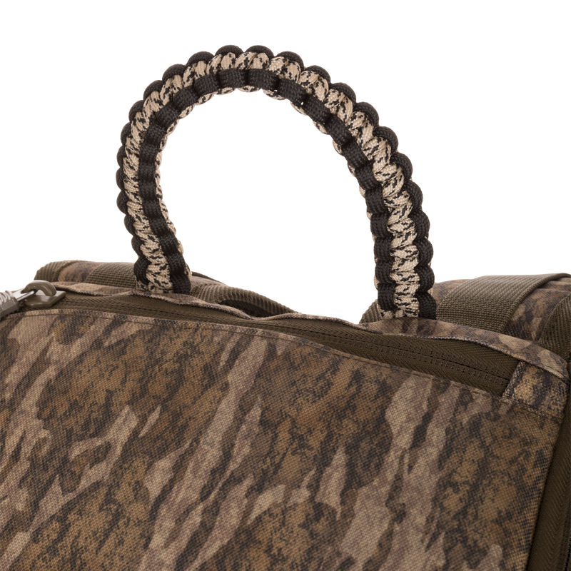 Close-up of the Tree Hugger Timber Pack showing its brown-and-green camo pattern, zippered pocket, and braided paracord carry-handle loop, emphasizing durability and organization.