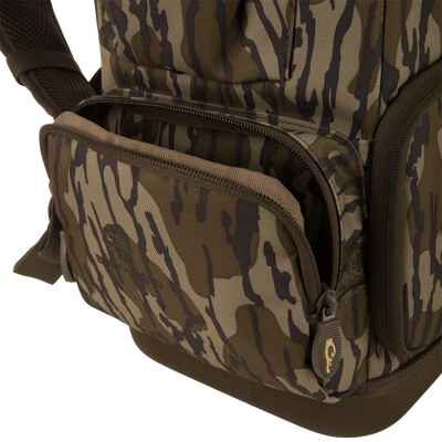Tree Hugger Timber Day Pack close-up shows camo design, front zippered pocket, main compartment zipper, and padded shoulder strap, highlighting its rugged, water-resistant features.