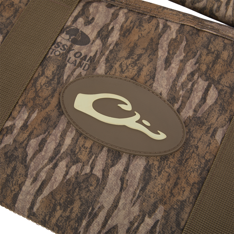 Migrator Gun Case close-up: camo-patterned fabric with olive-green straps and a brown C logo, highlighting durable, waterproof design for reliable firearm protection.