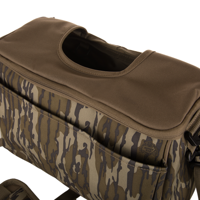Hardline Blind Bag close-up: camo-patterned, olive-green fabric with a top flap, front pocket, and shoulder strap, designed for waterfowl hunters' rugged, weather-resistant use.
