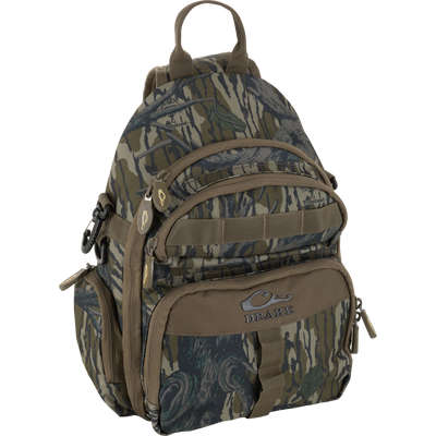Drake's Hardline Sling Pack, a camo-patterned, durable mini-backpack, features multiple zippered pockets, MOLLE webbing, and reinforced panels for rugged, weather-resistant outdoor use.