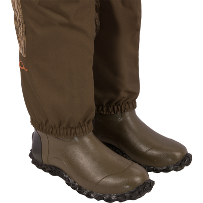 Close-up of legs in Hardline Breathable Youth Wader, showcasing waterproof fabric and elastic cuffs tucked into sturdy green rubber/neoprene boots, ideal for young outdoor enthusiasts.