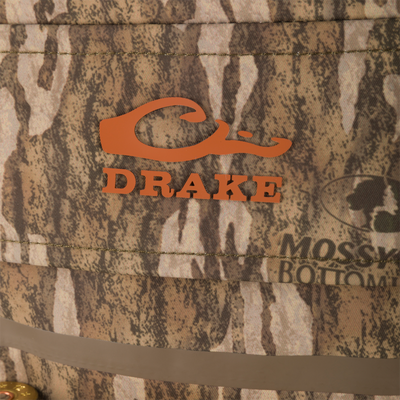 Drake Waterfowl camo hunting hat with orange logo, stitched brim, retention strap, and shotgun shell rim, complementing the Hardline Breathable Youth Wader's features.
