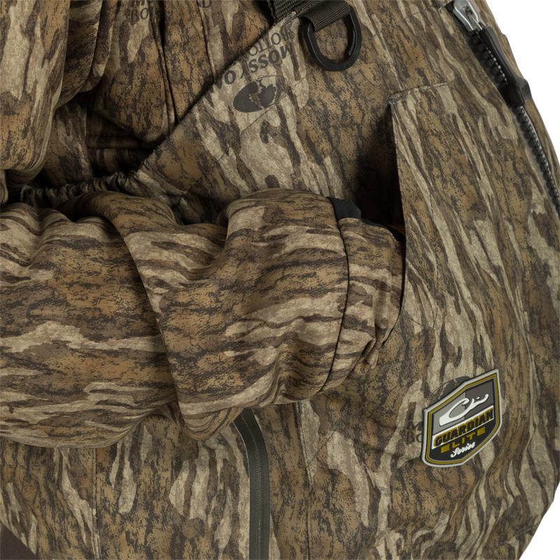 Uninsulated Guardian Elite HND Front Zip Waders - Green Timber: A person wearing a camouflage jacket with a close-up of a logo on the front.