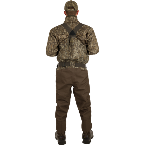A man in camouflage clothing wearing the Uninsulated Guardian Elite HND Front Zip Waders - Realtree, standing confidently in the outdoors.