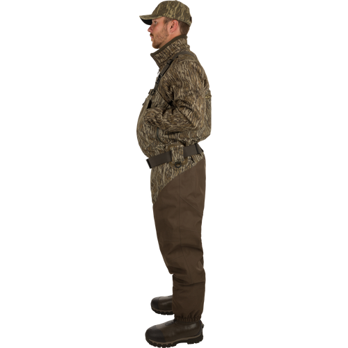 A man in camouflage clothing and hat wearing Uninsulated Guardian Elite HND Front Zip Waders - Realtree, standing confidently in the outdoors.