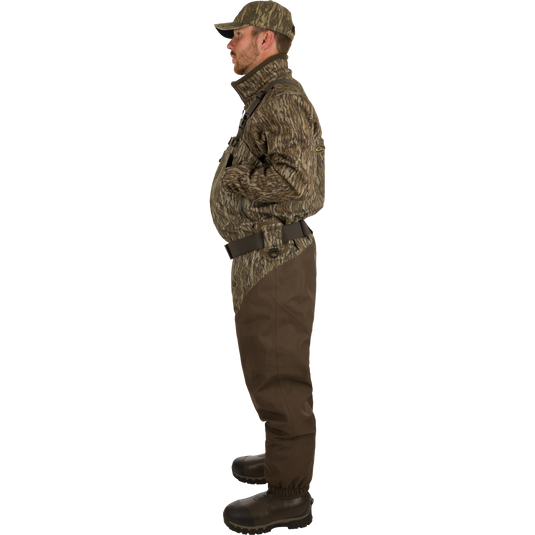 A man in camouflage clothing and hat wearing Uninsulated Guardian Elite HND Front Zip Waders - Habitat, standing confidently in the outdoors.