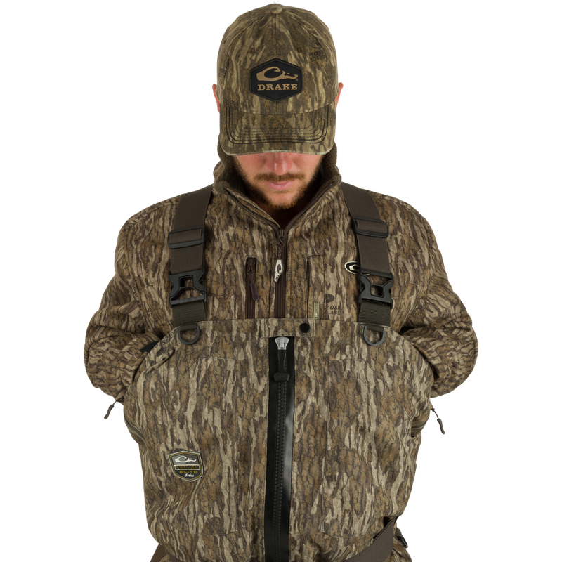 Uninsulated Guardian Elite HND Front Zip Waders - Green Timber: A man in a camouflage outfit wearing the waders, with a close-up of his face and a logo on the surface.