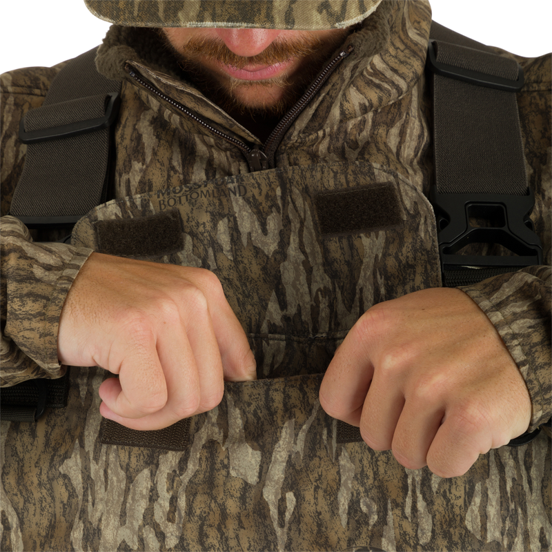 A man in camouflage clothing with hands in pockets, wearing Insulated Guardian Elite Vanguard Breathable Waders - Realtree.