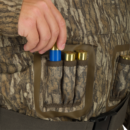 A person putting a blue and gold bullet into a belt on the Insulated Guardian Elite Vanguard Breathable Waders - Realtree.