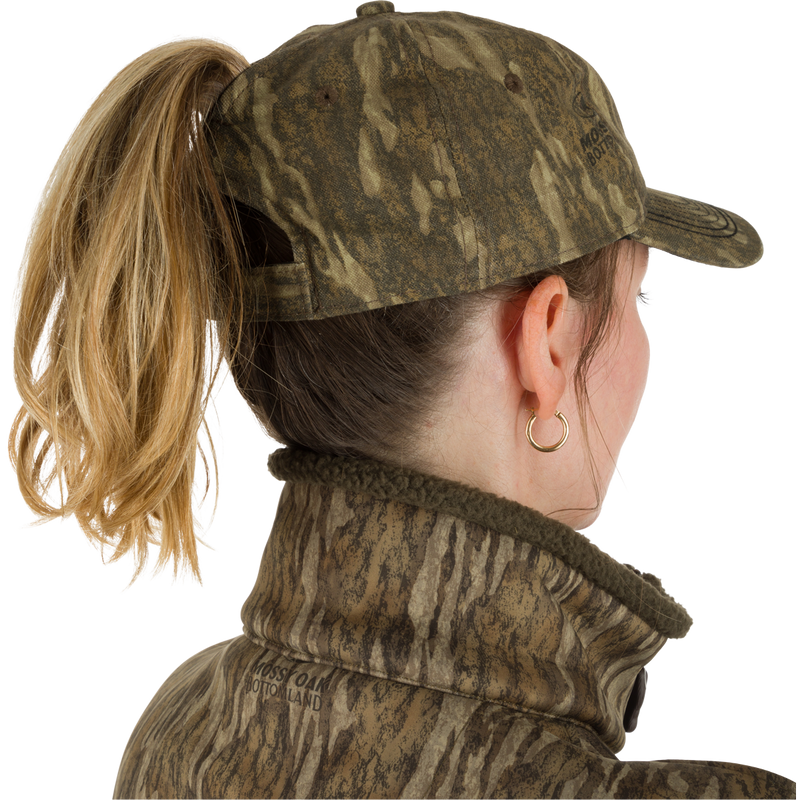 A woman wearing the Women's Camo Ponytail Cap, a low-profile hat with unstructured front panels and a hook-and-loop closure. The cap is made of a lightweight blend of 60% cotton and 40% polyester, and features a ponytail slot for freedom of movement. Perfect for tackling any terrain in style.