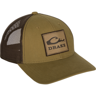 A weathered cotton/poly structured cap with a leather patch featuring the Drake Logo. Traditional trucker shape with a pre-curved visor and adjustable snapback closure. 