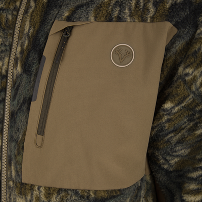 Close-up of the Non-Typical Statix Sherpa Fleece Insulated Jacket's tan soft-shell pocket flap with concealed zipper and antler logo, showcasing its rugged, weatherproof design.