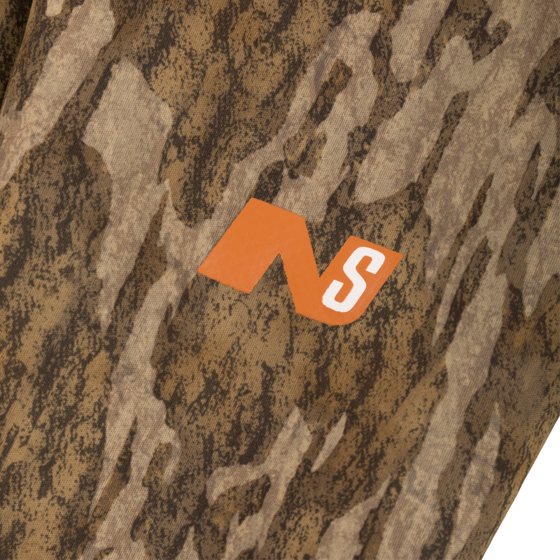 Close-up of the Midweight Nova Silencer Jacket's camouflage fabric with bright-orange NS logo, emphasizing its anti-odor, water-resistant features and practical design for hunting.
