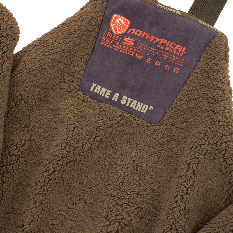 Close-up of Midweight Nova Silencer Bib with Scent Control featuring high pile sherpa fleece, orange non-typical by Drake patch, and chest pocket for outdoor enthusiasts.