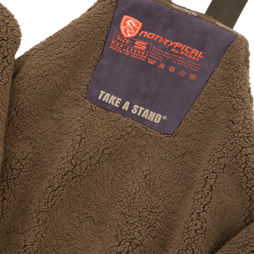 Close-up of Midweight Nova Silencer Bib with Scent Control featuring high pile sherpa fleece, orange non-typical by Drake patch, and chest pocket for outdoor enthusiasts.