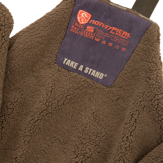 Close-up of Midweight Nova Silencer Bib with Scent Control featuring high pile sherpa fleece, orange non-typical by Drake patch, and chest pocket for outdoor enthusiasts.
