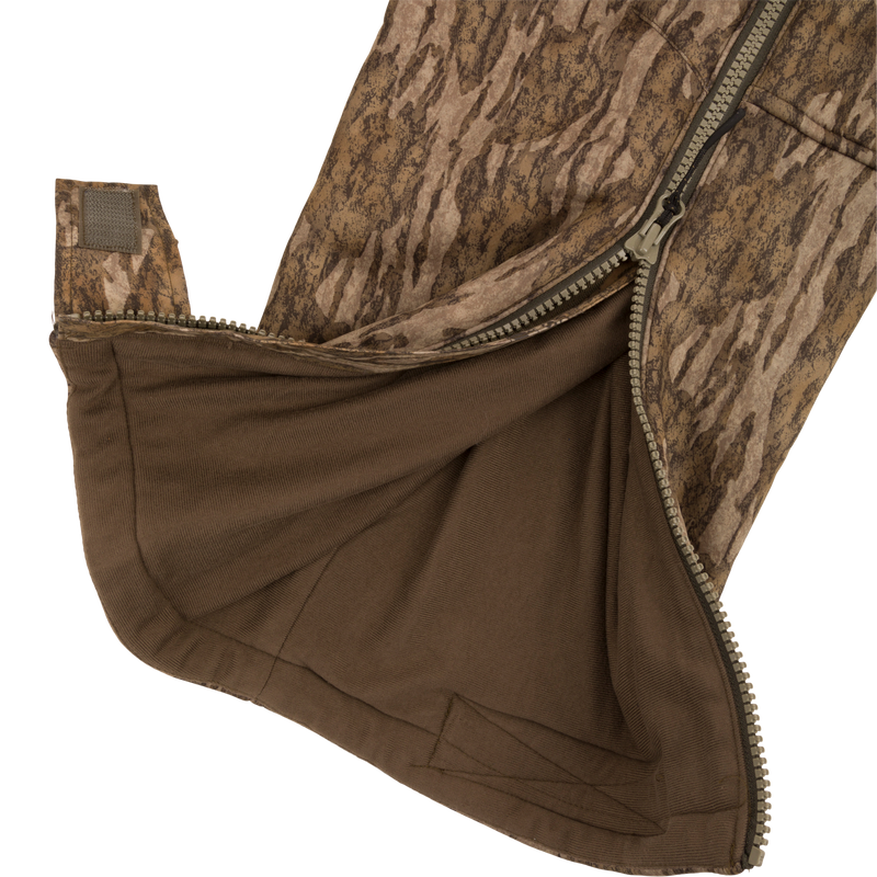 Close-up of the Midweight Nova Silencer Bib with Scent Control, showing the camo gaiter section, partially unzipped to reveal brown inner lining and adjustable Velcro tab.