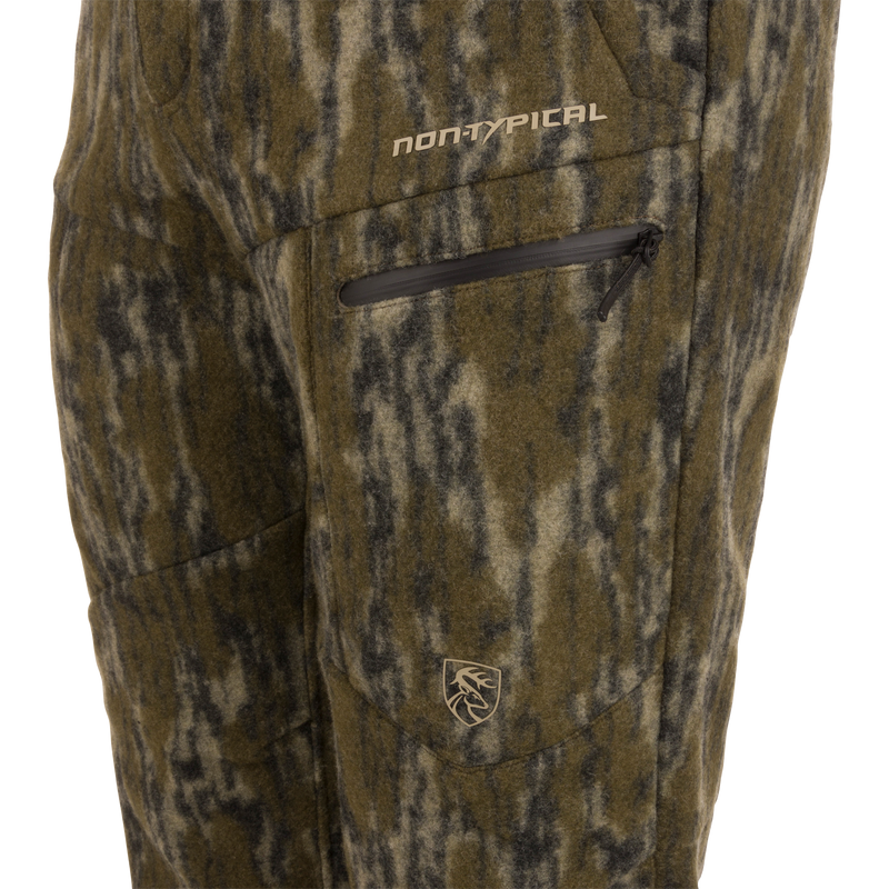 Close-up of Midweight Hydrowool Softshell Pant with Scent Control, featuring a camouflage-patterned fleece, zippered pocket with “NON-TYPICAL” text, and deer head logo.