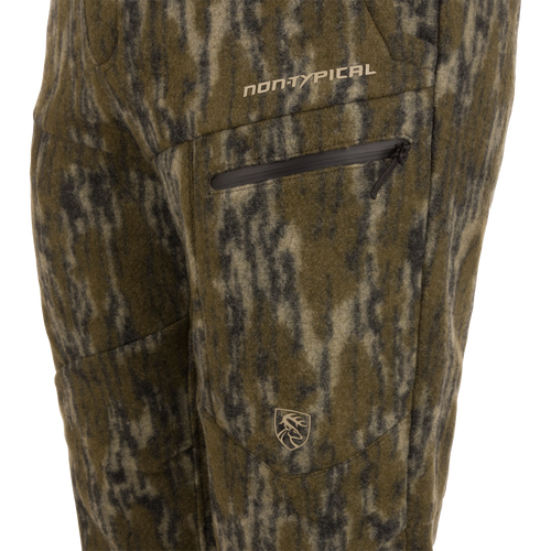 Close-up of Midweight Hydrowool Softshell Pant with Scent Control, featuring a camouflage-patterned fleece, zippered pocket with “NON-TYPICAL” text, and deer head logo.